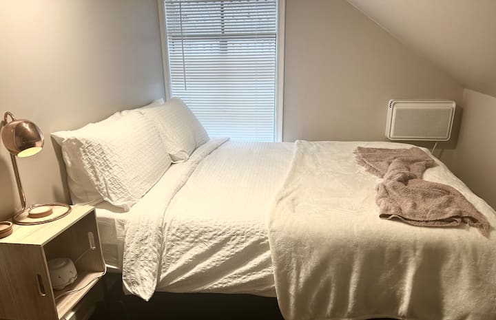 The queen bed offers a luxurious sleeping experience with a comfortable mattress and high-quality linen, ensuring a restful night's sleep for guests. The lamp and sound machine adds to the comfort of home.