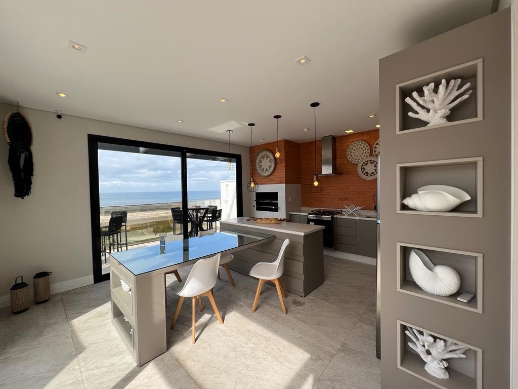 The modern kitchen showcases a spacious island with a sleek countertop. Large glass doors provide a view of the outdoor space, while light fixtures hang elegantly above. Decorative elements are displayed on the walls, emphasizing a coastal theme in the design.