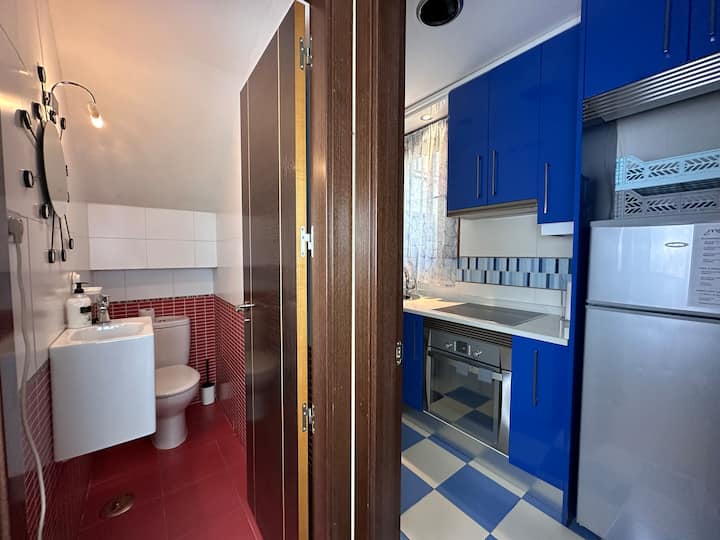 Cocina en azul con horno, nevera y aseo contiguo: moderna y totalmente equipada.
