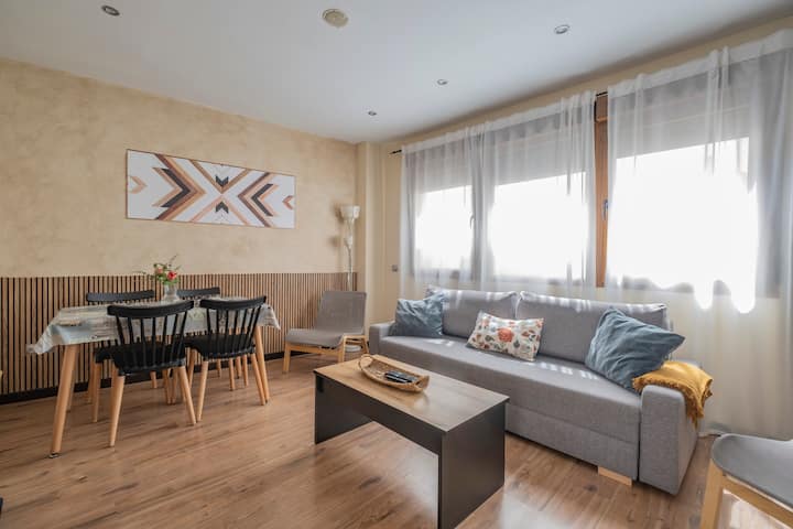 Salón-comedor con sofá, mesa de diseño y ventanales: ambiente moderno y confortable.