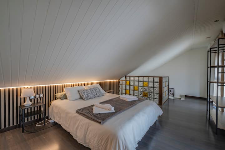 Dormitorio 1 con cama de matrimonio y luz cálida bajo el techo inclinado: moderno y confortable.