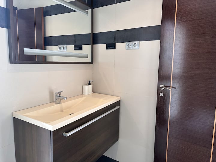 Baño con mueble de madera, espejo grande y lavabo: elegante y funcional.