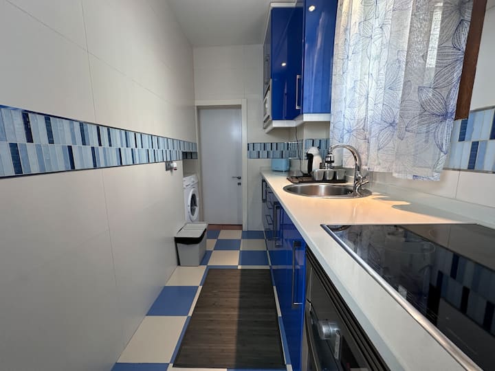 Cocina alargada en azul con vitrocerámica y lavadora: funcional y muy luminosa.