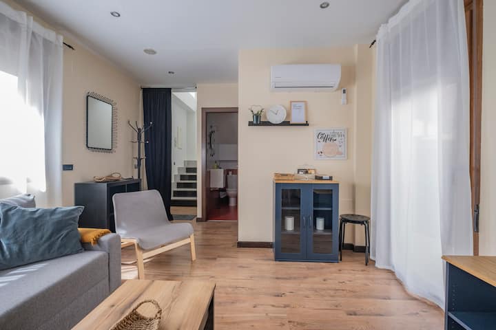 Salón con butacas, aparador y escalera al fondo: acogedor y con mucha luz natural.
