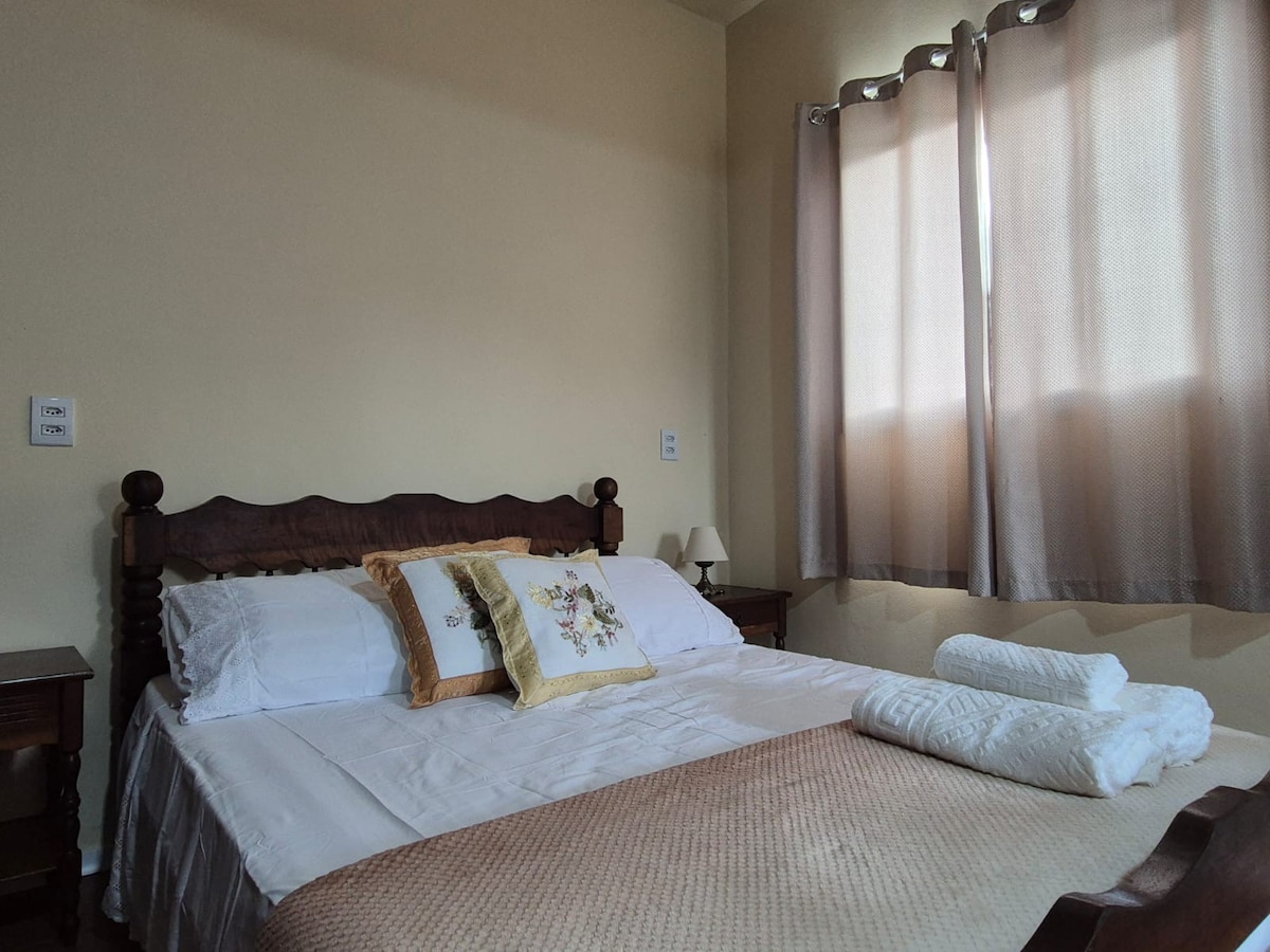 A well-appointed bedroom features a spacious bed with decorative pillows, complemented by crisp linens. Natural light filters through sheer curtains, illuminating the warm walls. Nightstands are positioned on either side of the bed, enhancing the cozy atmosphere.