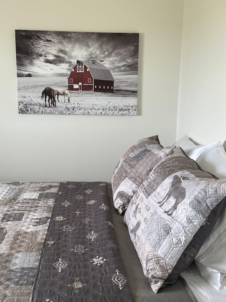 Welcome to the second bedroom, featuring a cozy queen-size bed adorned with a rustic quilt cover. The charming red barn artwork adds a touch of countryside charm, making this a delightful retreat for your stay