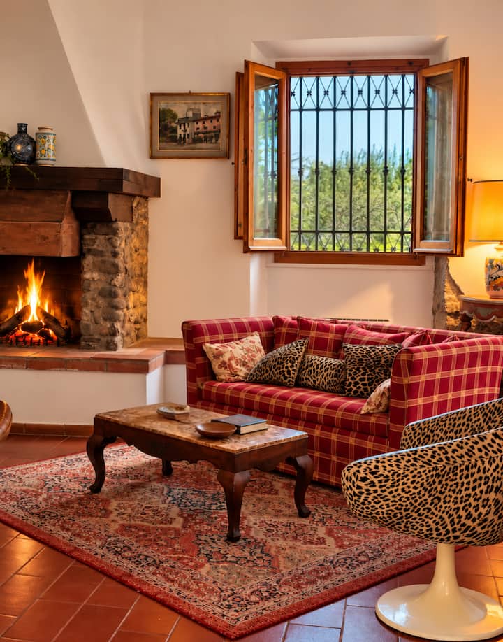 Cozy up in this charming living room! Yet a another space to enjoy your stay. Rustic stone fireplace, plush red plaid sofa, & vintage rug create a warm atmosphere. Unwind and gaze out at the greenery. Perfect quaint retreat to feel at home.
