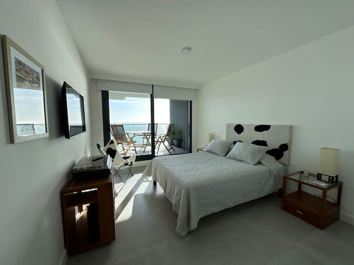 Habitación principal en suite con terraza y vistas al mar, cómoda cama matrimonial, placar y TV
