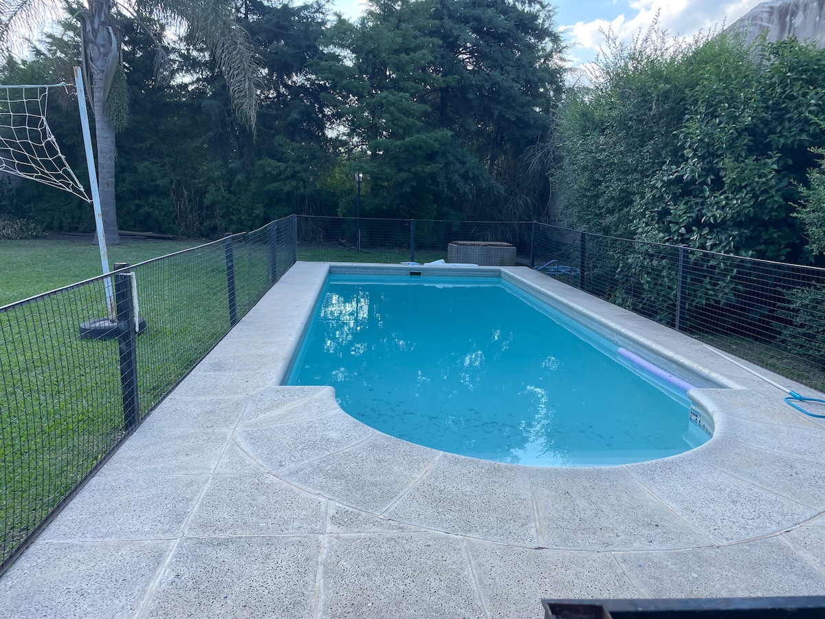 A refreshing pool is set within a spacious outdoor area, surrounded by a safety fence. Lush greenery is visible in the background, contributing to a serene environment. The pool features a gently sloping entrance, ideal for relaxation and leisure.