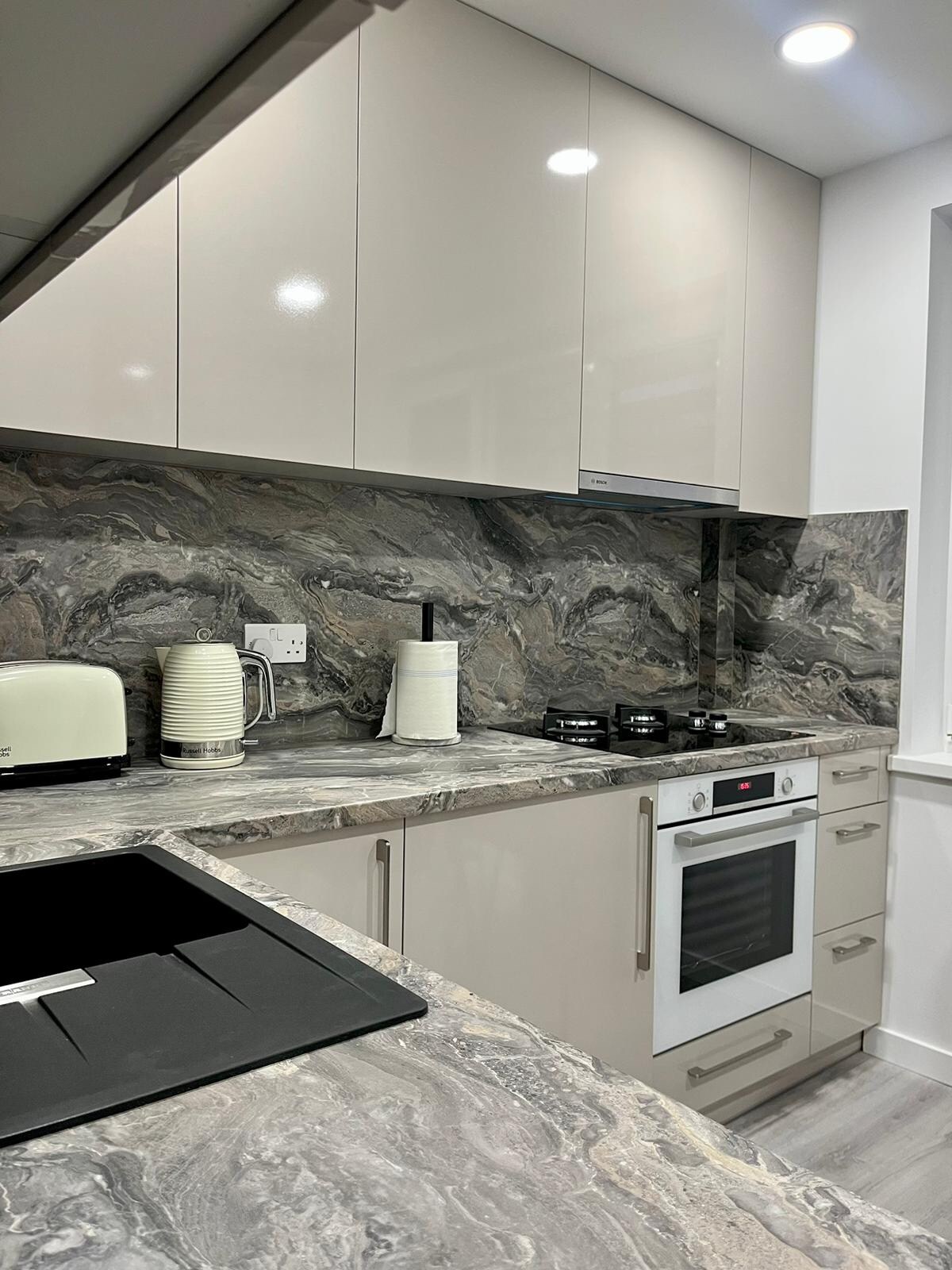 A modern kitchen features sleek cabinetry and a striking marble backsplash. High-end appliances, including a stovetop and oven, complement the elegant design. A light-colored toaster sits on the countertop, enhancing the overall aesthetic of the space.