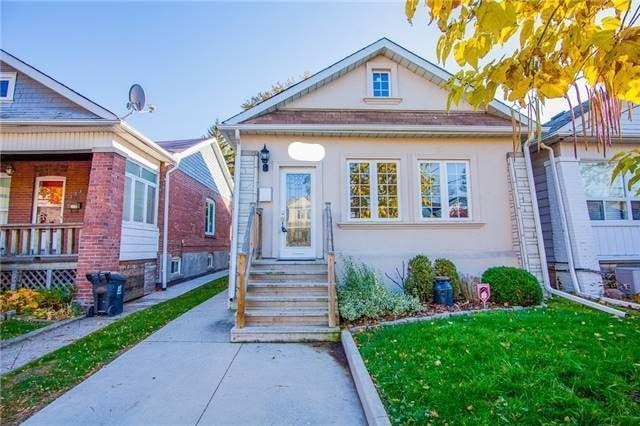 A charming bungalow is represented, featuring a well-maintained exterior with a welcoming entrance. The steps lead to a front door framed by large windows that allow natural light to illuminate the porch area. Lush greenery and a manicured lawn complement the inviting appeal of the home.