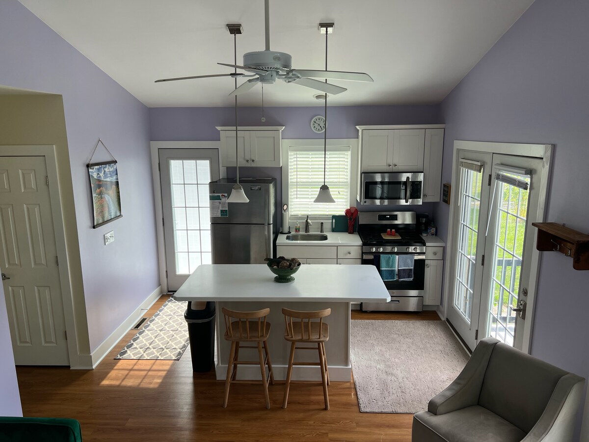 A well-equipped kitchen features modern appliances, including a stove and refrigerator. Ample counter space is provided, along with two wooden stools at the island. Natural light filters through the two sets of French doors, creating a bright and inviting cooking area.