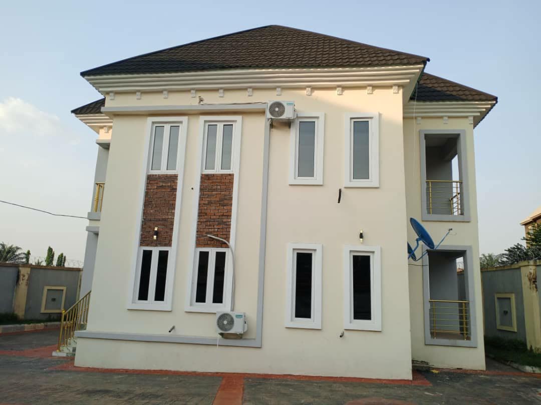 The exterior of the two-story house showcases a modern design with a light-colored facade and a combination of brick and smooth walls. Large windows enhance natural light, while the balcony features a railing. Air conditioning units are mounted on the sides for comfort.