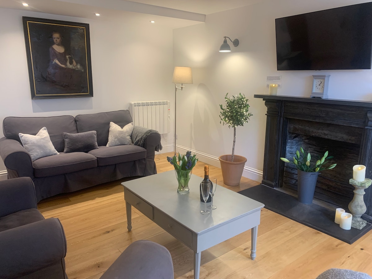 A cozy living area is highlighted by a comfortable gray sofa adorned with decorative cushions. A wooden coffee table is centered beneath a wall-mounted television. A potted plant adds a touch of greenery, while a fireplace features candles in a stylish arrangement.