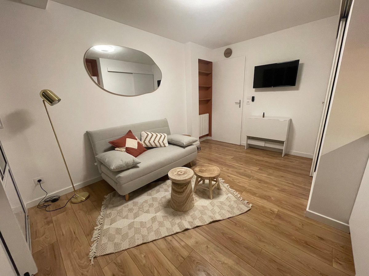 A light-infused living area features a gray sofa adorned with decorative cushions. A wooden coffee table and a textured rug enhance the space. A wall-mounted television is positioned above a modern console. Soft lighting is provided by a standing lamp, contributing to a cozy ambiance.