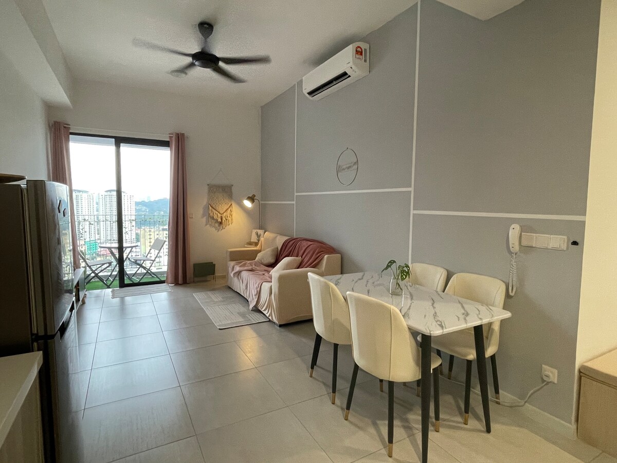 A modern living space is displayed, featuring a comfortable sofa and a dining table set for four. Large sliding doors provide access to a balcony with city views. Light-colored walls and a neutral color palette enhance the bright and airy feel of the room.