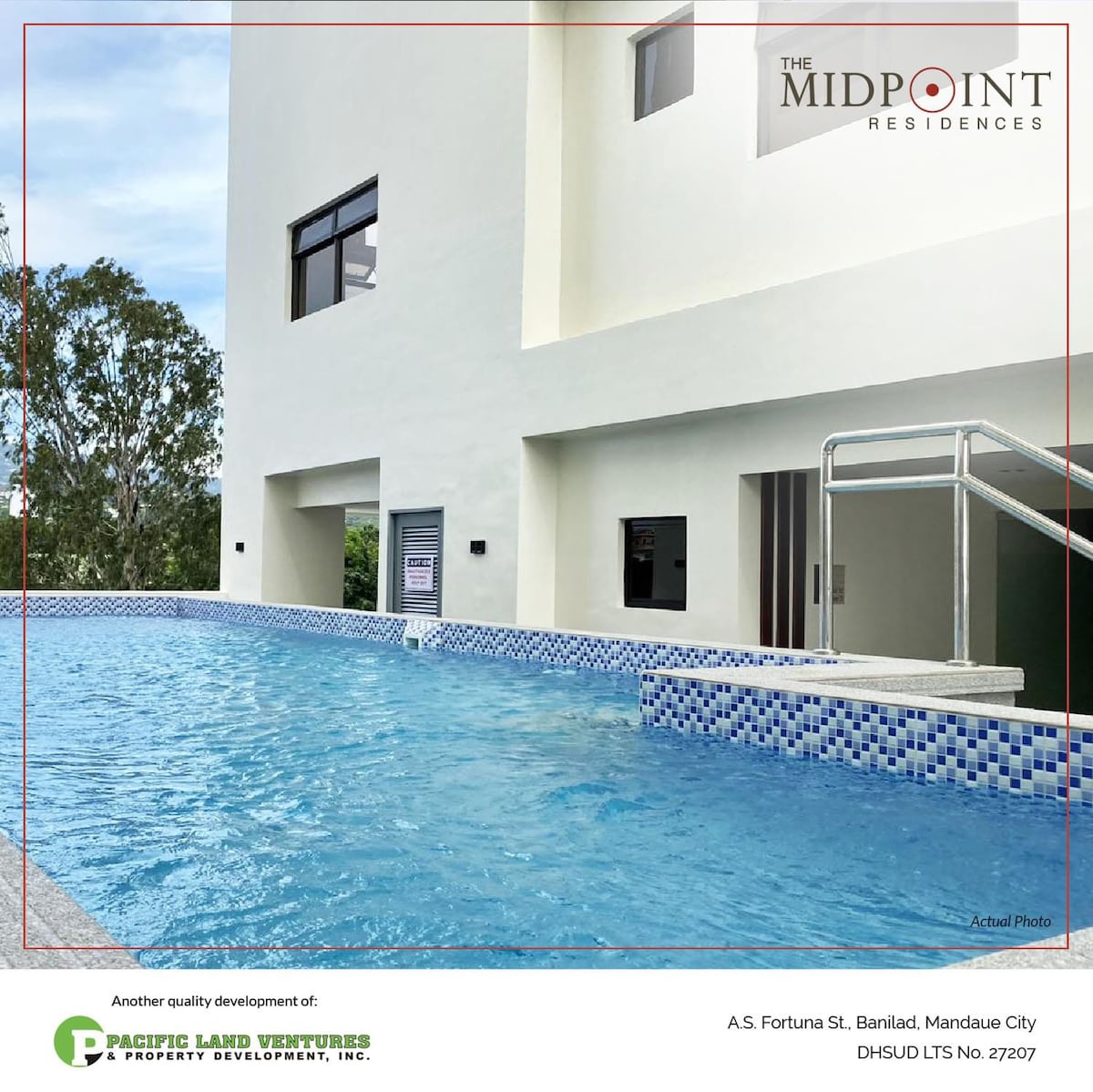 A serene swimming pool is presented, featuring clear blue water and a tiled edge. The pool is framed by the contemporary architecture of the building, which includes large windows and a well-maintained surrounding area with lush greenery.
