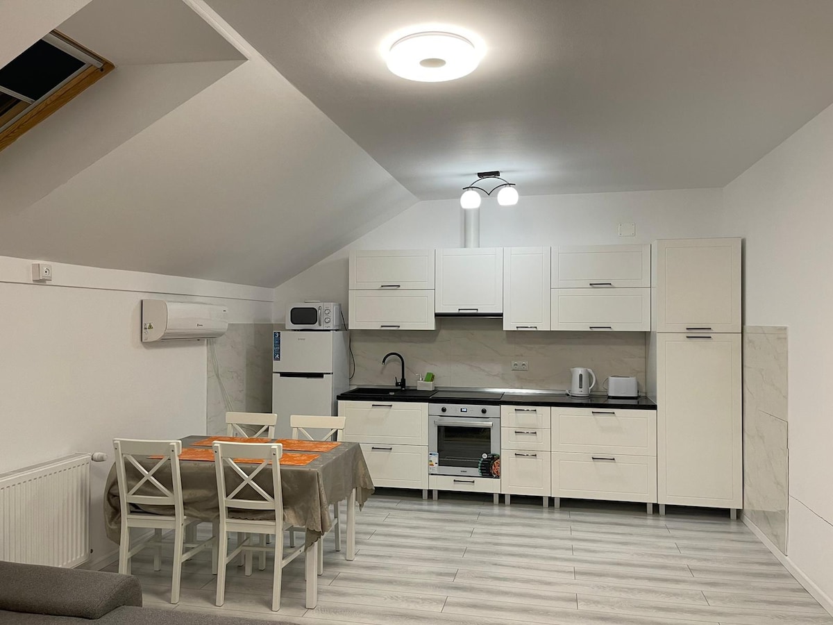 An open-concept kitchen and dining area features sleek white cabinetry and modern appliances. A round dining table with four chairs is positioned under a contemporary light fixture, while a skylight provides natural light to the space.