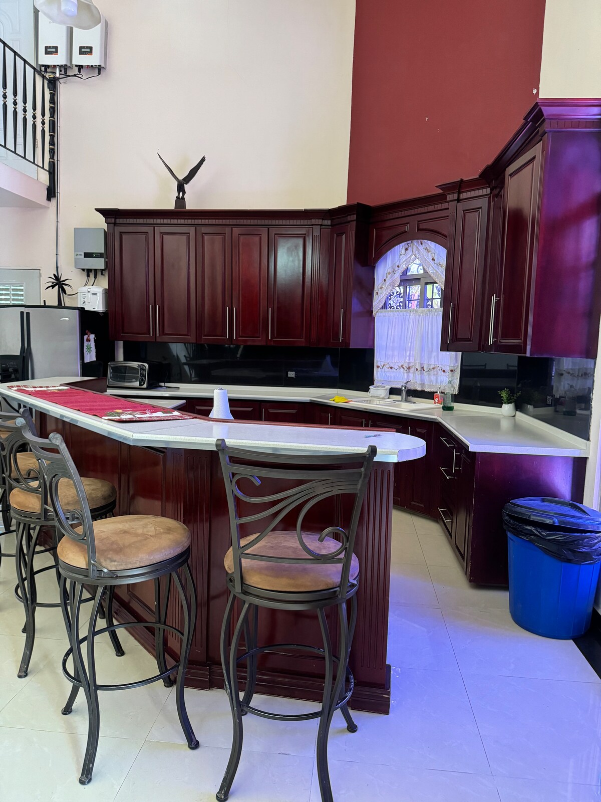 The kitchen features rich, dark cabinetry with a modern countertop. A breakfast bar with high stools provides seating for five. A window allows natural light to fill the space, while kitchen appliances are neatly positioned for convenience.