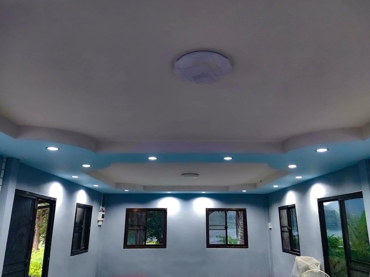 The interior space features a modern ceiling design with soft blue accents and recessed lighting. Multiple light fixtures provide ample illumination, while large windows framed in black allow natural light to fill the room. The walls are a neutral tone, enhancing the spacious feel.
