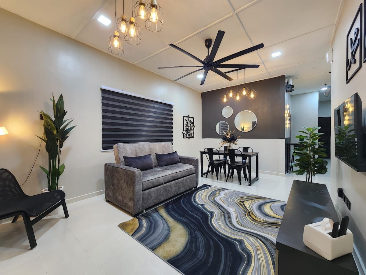 The living hall features a comfortable sofabed and a stylish dining area with a table for four. Soft lighting is provided by hanging fixtures, and a ceiling fan promotes air circulation. Decorative plants add a touch of greenery to the modern and minimalist design.