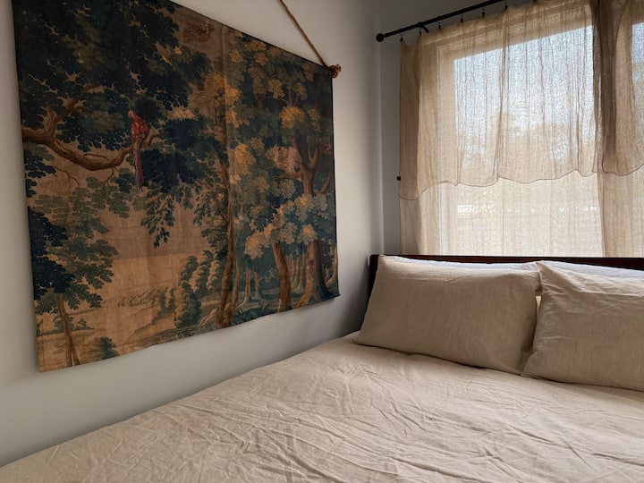 Relax in our small and cosy bedroom, complete with a queen-size bed dressed in luxurious linen and a gorgeous wall hanging, perfect for a restful retreat.