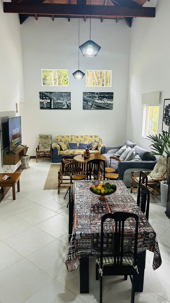 Sebule iliyo na sofa ya viti 3, televisheni ya "65" na kitanda cha sofa.  Sehemu ya mbele, chumba cha kulia chakula chenye meza ya viti 6