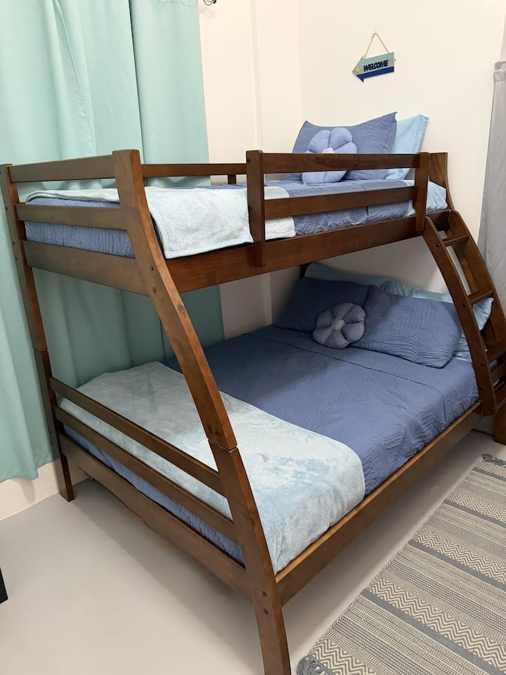 The first bedroom has a closet, luggage rack, lap desk, hangers, and a full-length mirror behind the door. It features a bunk bed with one single and one double bed, accommodating up to three people, and cooling memory foam mattresses for comfort.