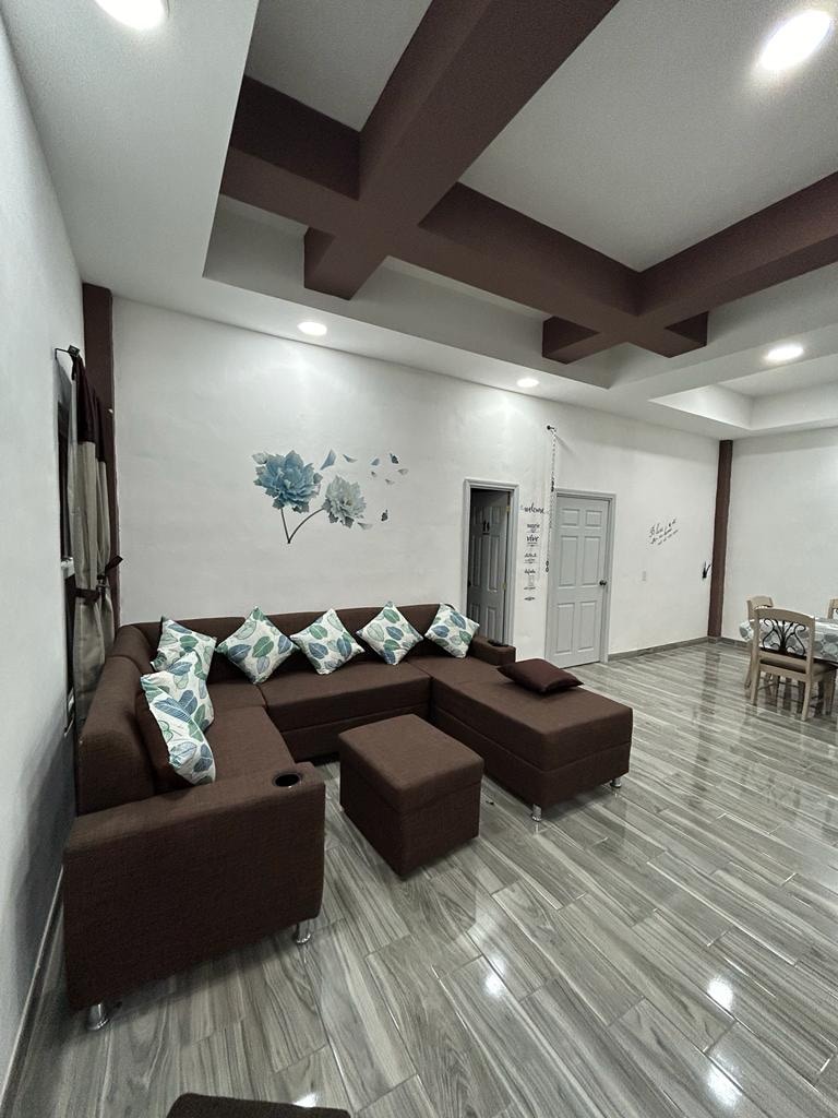 A modern living area is showcased, featuring a spacious sectional sofa adorned with decorative cushions. Light-colored walls and hardwood floors complement the earthy tones of the furniture. A wall art piece adds a subtle decorative element, while the room is illuminated by recessed lighting.