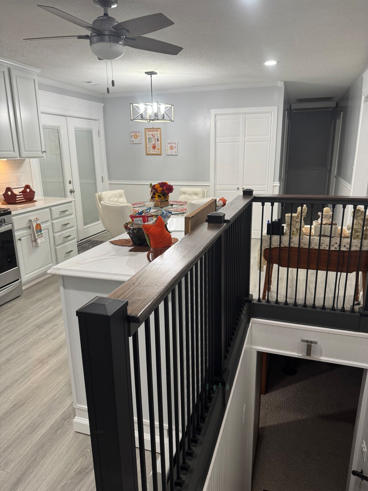 A view from the second floor showcases the modern kitchen and living area below. The kitchen features white cabinetry and sleek appliances, while a cozy seating arrangement is visible. A decorative arrangement of flowers adds a pop of color to the dining area.