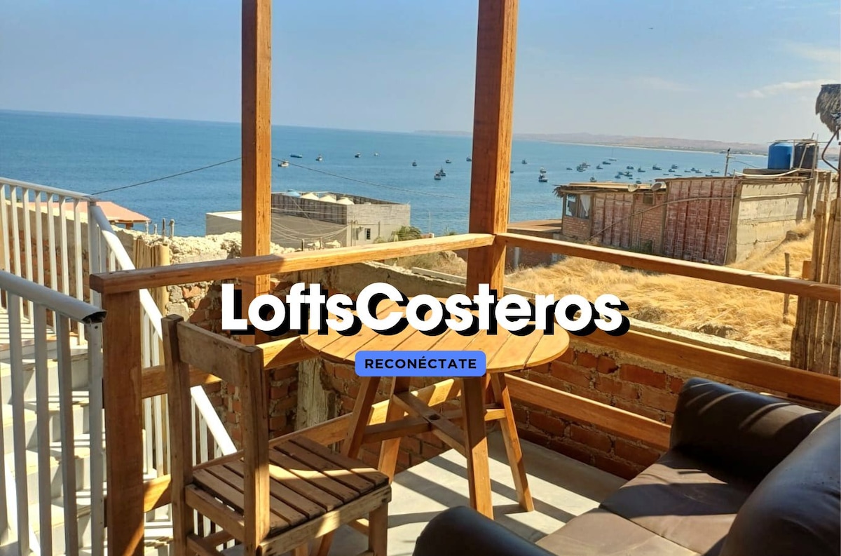 An outdoor balcony offers a scenic view of the ocean, with wooden furniture positioned for relaxation. The horizon displays a clear sky, and subtle waves can be seen in the water. Nearby boats are visible, contributing to the coastal atmosphere.