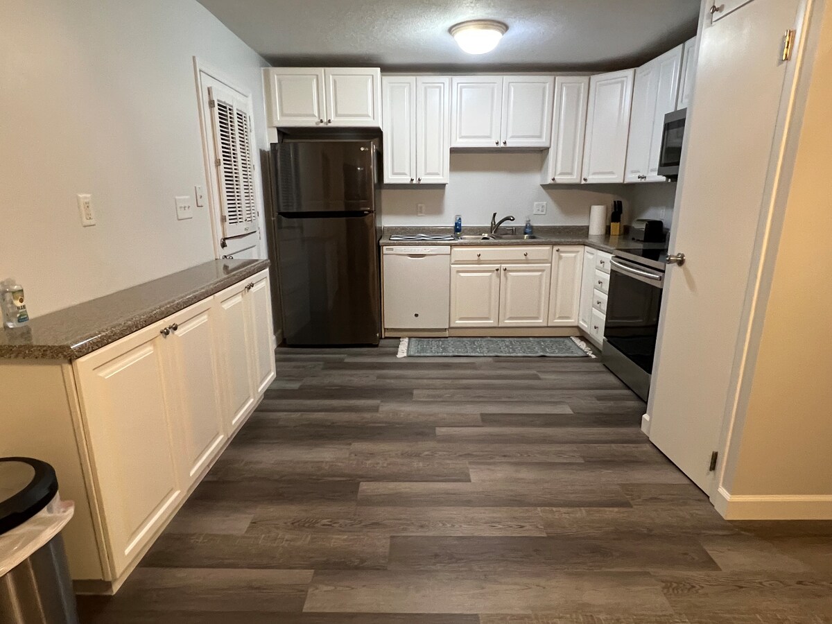 The kitchen features white cabinetry and silver appliances, including a refrigerator, oven, and microwave. A granite countertop separates the kitchen from the dining area. The floor is designed with wood-like tiles, contributing to a contemporary and functional space.