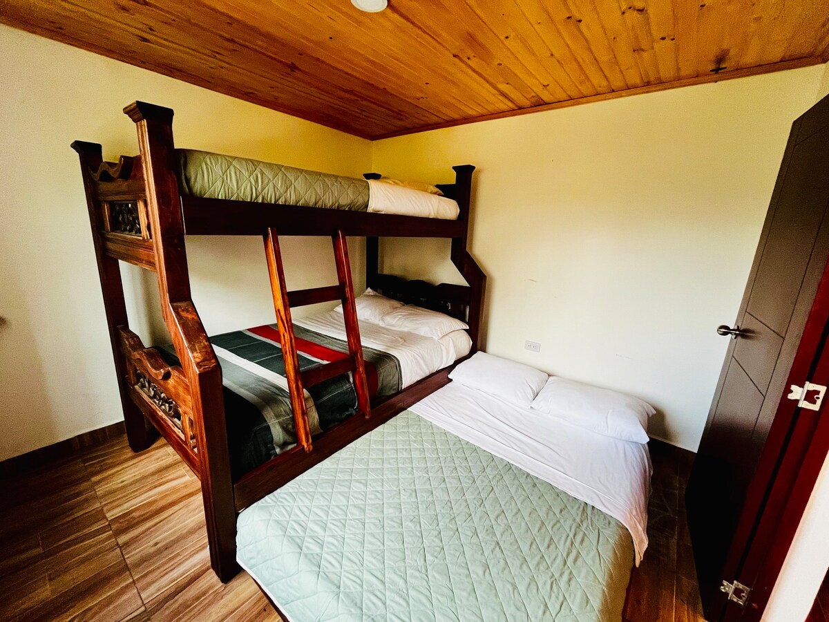 A multi-level sleeping arrangement is showcased, featuring a sturdy wooden bunk bed. The lower level contains a spacious mattress, while the upper level offers another mattress. Soft bedding in neutral tones is present, complementing the wooden walls and ceiling.
