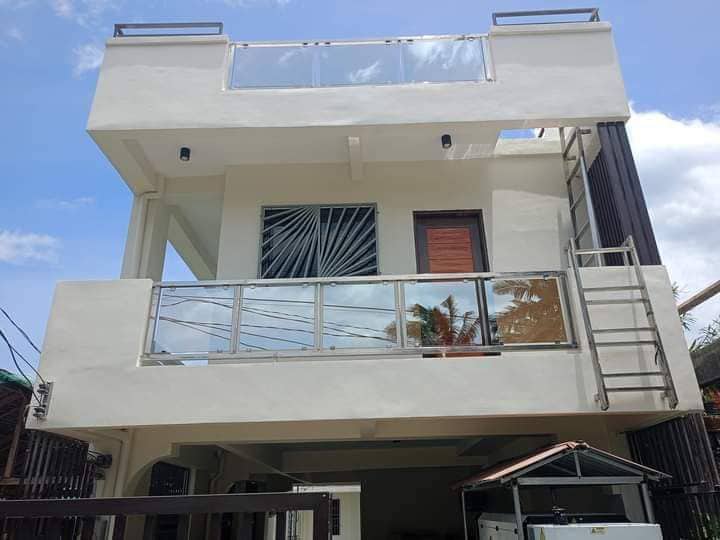 A modern two-story building is depicted, featuring a spacious balcony with glass railings. A large window allows natural light into the interior, while a staircase provides access to the upper level. The facade is characterized by clean lines and a neutral color palette.