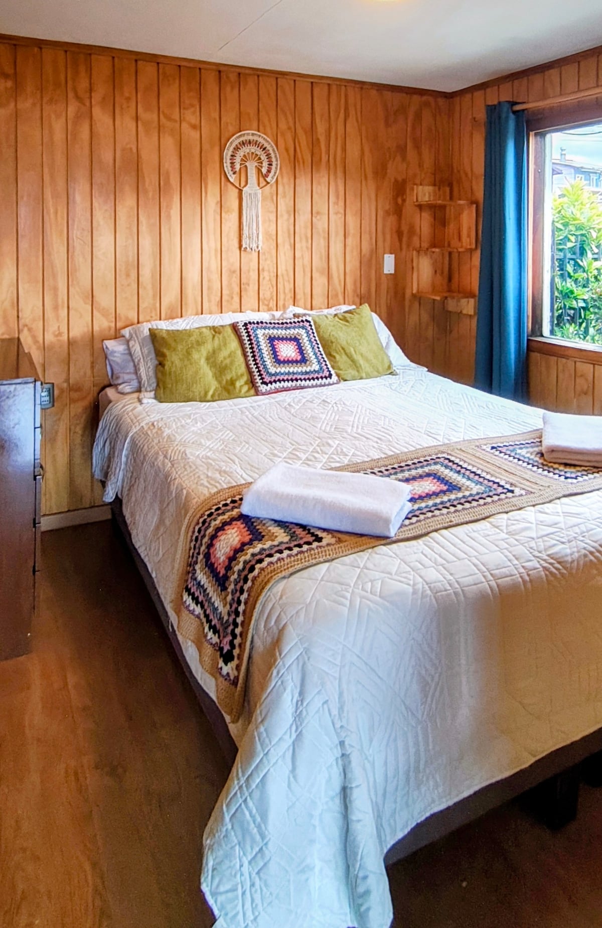 Удобна и светла спална соба со брачен кревет и рачно изработени детали. Дрвените ѕидови и ткаените ќебиња создаваат топла и јужна атмосфера, идеална за одмор по разгледувањето на Пуерто Варас.
