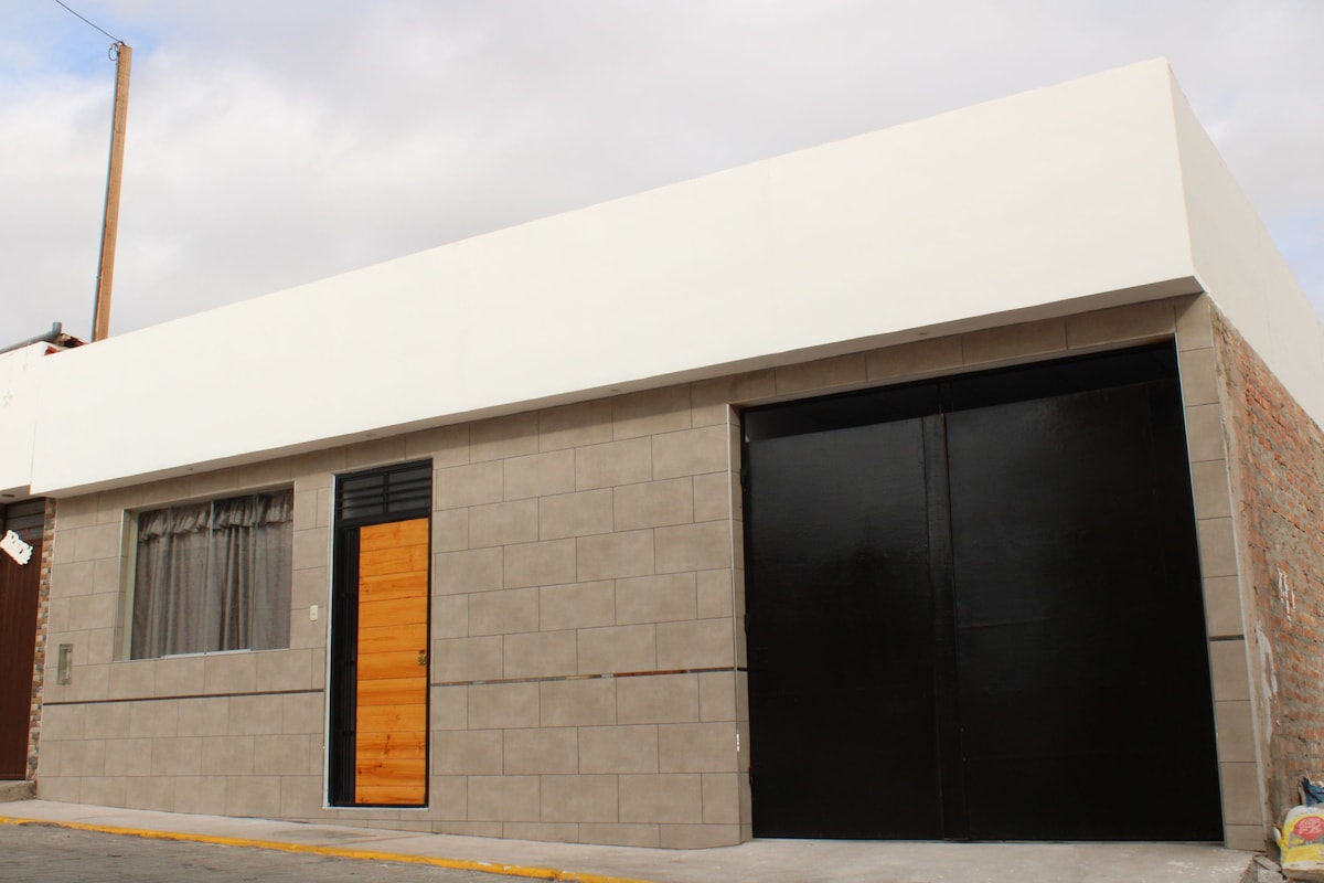 The exterior of the property showcases a modern design with a smooth white facade and contrasting dark garage door. A wooden front door adds warmth to the entrance, while a large window is visible, adorned with soft curtains.