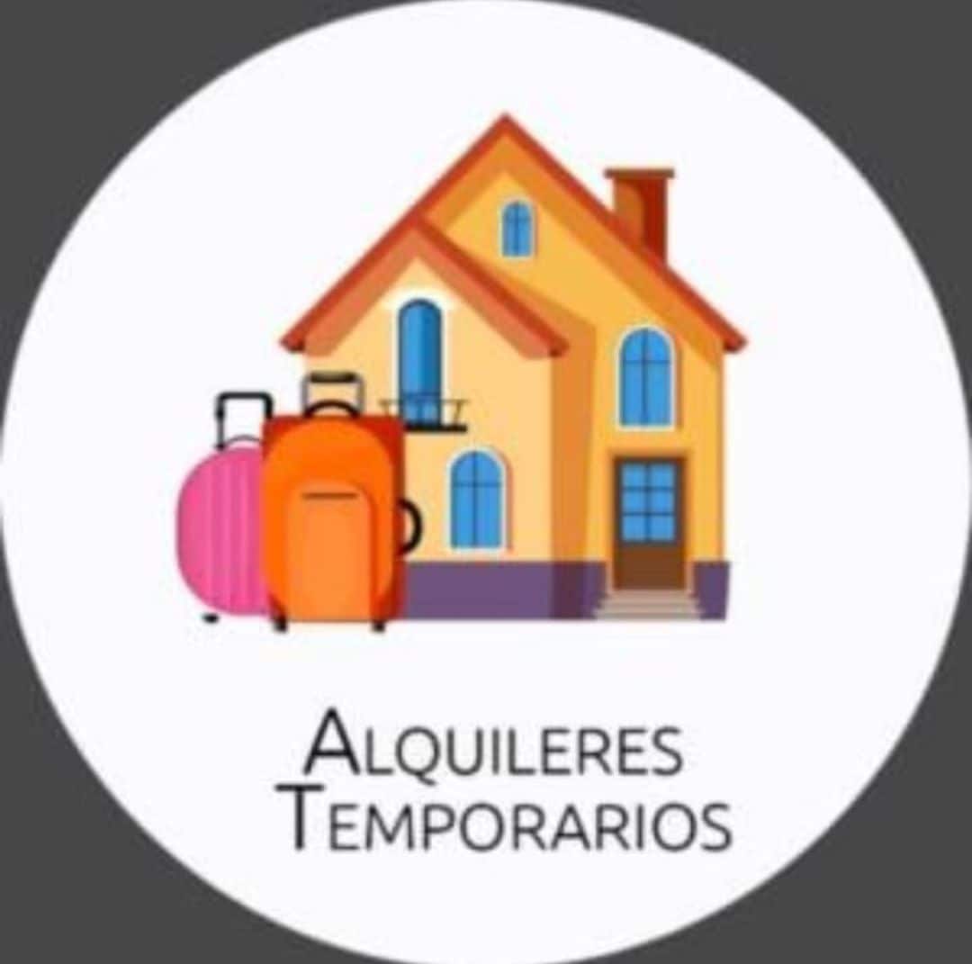 A graphic image depicting a stylized house with a welcoming design. Two vibrant suitcases in shades of pink and orange are positioned beside the home, indicating a focus on temporary rentals.