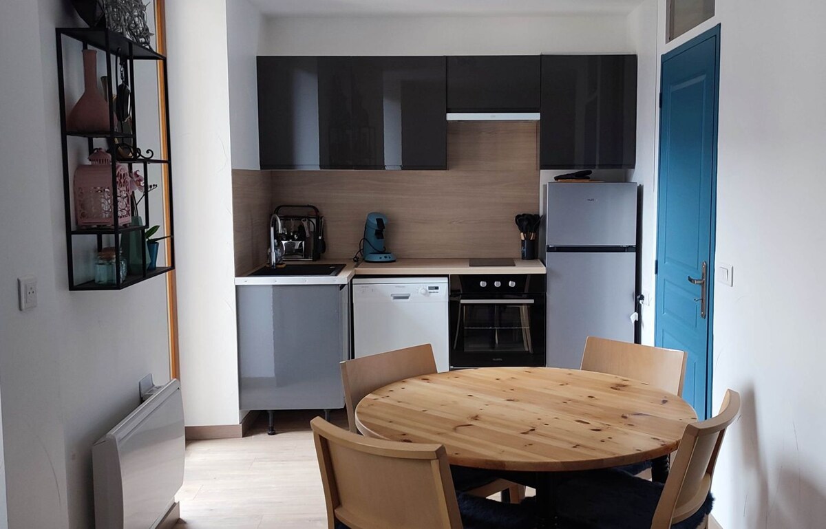 A modern kitchen area showcases sleek, dark cabinets complemented by a wooden dining table surrounded by four chairs. Appliances include a refrigerator, dishwasher, and oven, creating a functional and inviting space. Natural light enters through a nearby window, enhancing the bright atmosphere.