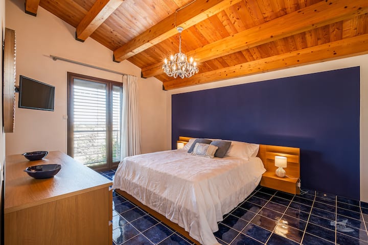 غرفة نوم رئيسية أنيقة وواسعة بإطلالة جميلة على البحر. تتميز هذه الغرفة بسقف خشبي مشع ولمسات زرقاء عميقة، وتنضح بالدفء والهدوء. استيقظ على الضوء الطبيعي اللطيف وسحر البحر المهدئ، المرئي من بعيد.