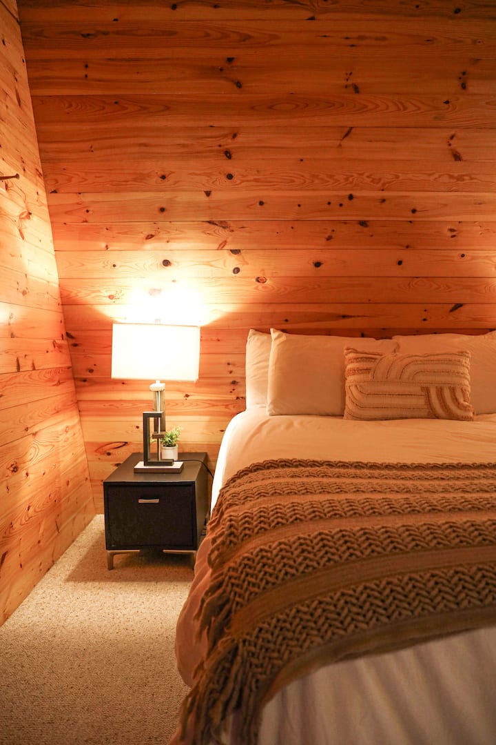 Manželská posteľ s útulnou posteľnou bielizňou, nočným stolíkom a lampou.