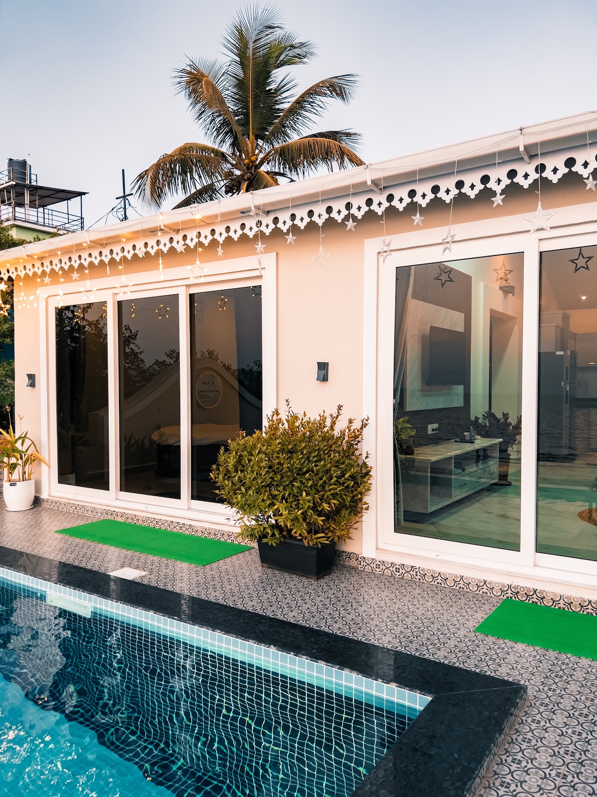 A private pool is framed by stylish tiles and potted plants. Expansive glass doors invite natural light into the villa, while palm trees add a tropical touch. The outdoor area offers a serene setting with easy access to indoor living spaces.
