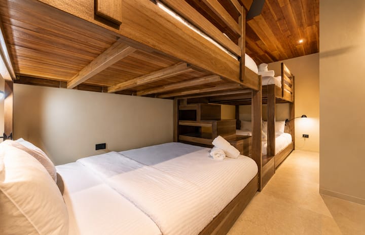 Isang iniangkop na kuwartong may bunk bed na idinisenyo para sa mga pamilya at grupo, na may 2 gawang-kamay na kahoy na bunk bed, mga premium na queen‑size na kutson na katulad ng nasa hotel, mainit na ambient lighting, at komportableng modernong disenyo na magugustuhan ng mga bata at matatanda