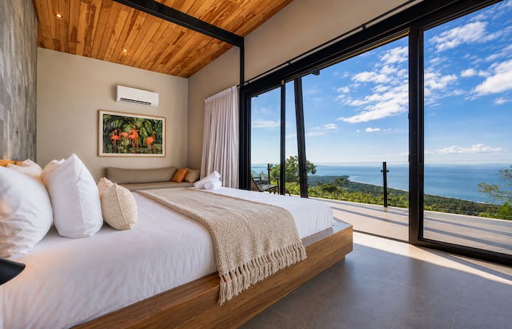 Gumising nang may mga panoramic na tanawin ng Karagatang Pasipiko mula sa komportableng king‑size na higaan mo. Malambot at marangyang linen, orihinal na likhang‑sining na tropikal, at floor‑to‑ceiling na salamin ang bumubuo sa payapang bakasyunan na napapaligiran ng likas na ganda ng Costa Rica