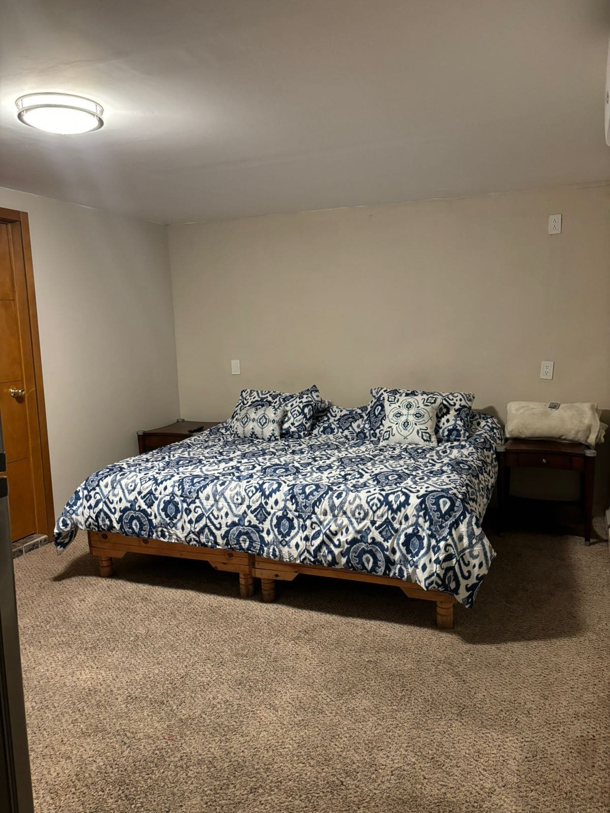 A bedroom features a spacious bed with a blue and white patterned quilt, accompanied by matching pillows. Two nightstands are positioned on either side, adding functionality to the room. The walls are painted a neutral color, and soft carpet covers the floor.