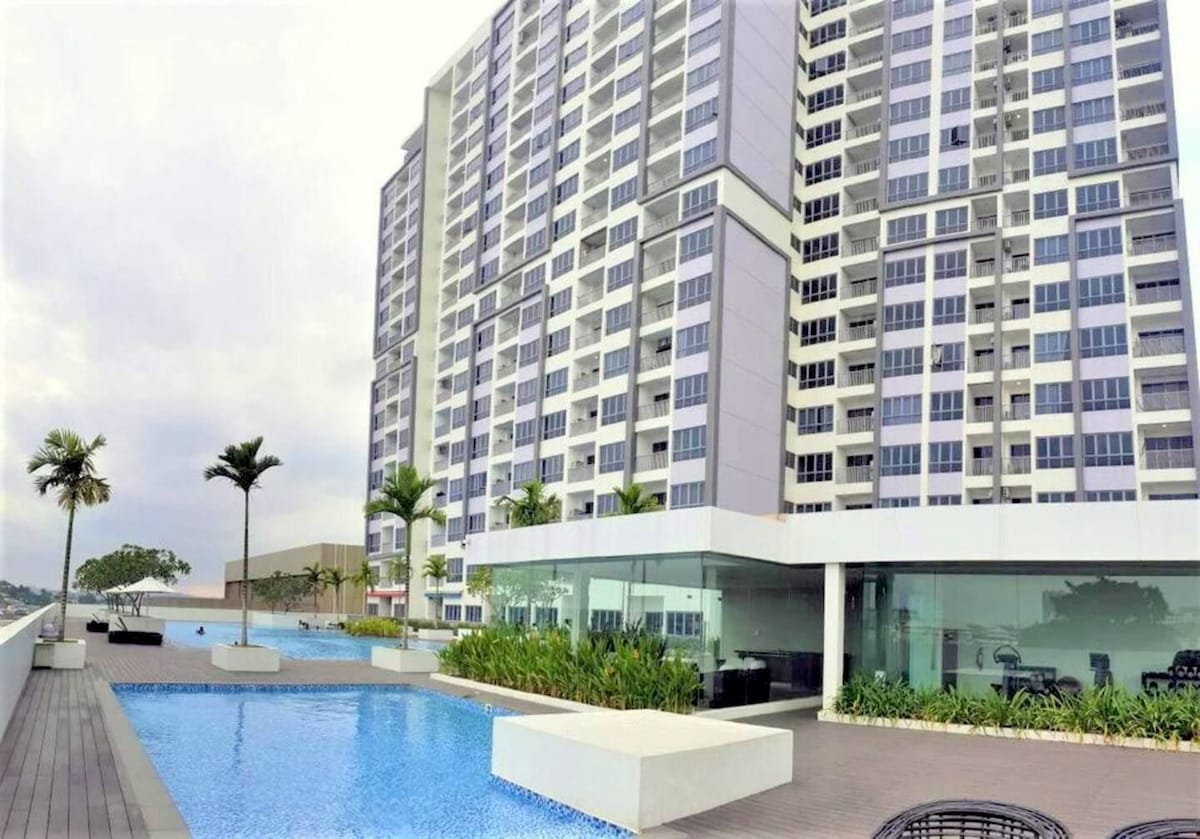 A modern residential building with multiple stories is depicted, featuring a lovely outdoor swimming pool surrounded by landscaped greenery. Palm trees are visible near the pool area, creating a tropical feel. The building's facade showcases large windows that enhance natural light.