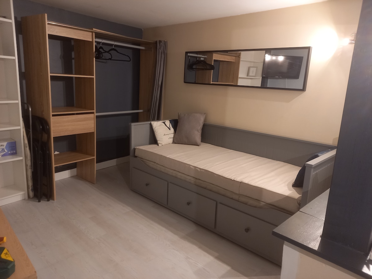 A simple sleeping area features a versatile bed that can accommodate one or two guests. Storage drawers are integrated beneath the bed. A mirror is mounted on the wall, reflecting the organized space, which includes a closet with hangers and open shelving.