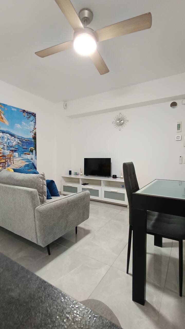 მთავარი მისაღები ოთახი, თანამედროვე და მყუდრო მისაღები ოთახი ნაცრისფერი დივნით, ტელევიზორით, სასადილო მაგიდით და ჭერის ვენტილატორით. ელეგანტური დეკორი და ნათელი გარემო იდეალურია დასასვენებლად ან წყვილებისთვის. სასადილო ოთახი, სამზარეულოთი.