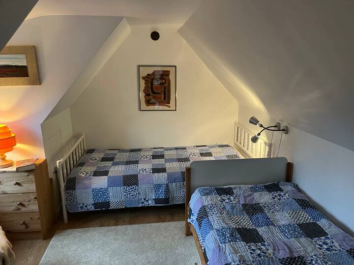 في غرفة في الطابق العلوي، يوجد سريران مفردان وزاوية قراءة تطل على المدخل.