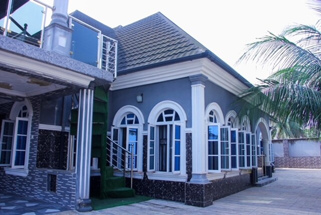 The exterior of the property features an elegant design with multiple arched windows, allowing natural light to fill the space. A green staircase leads to an upper level, framed by palm trees that add a tropical feel. A spacious courtyard is visible in the foreground.