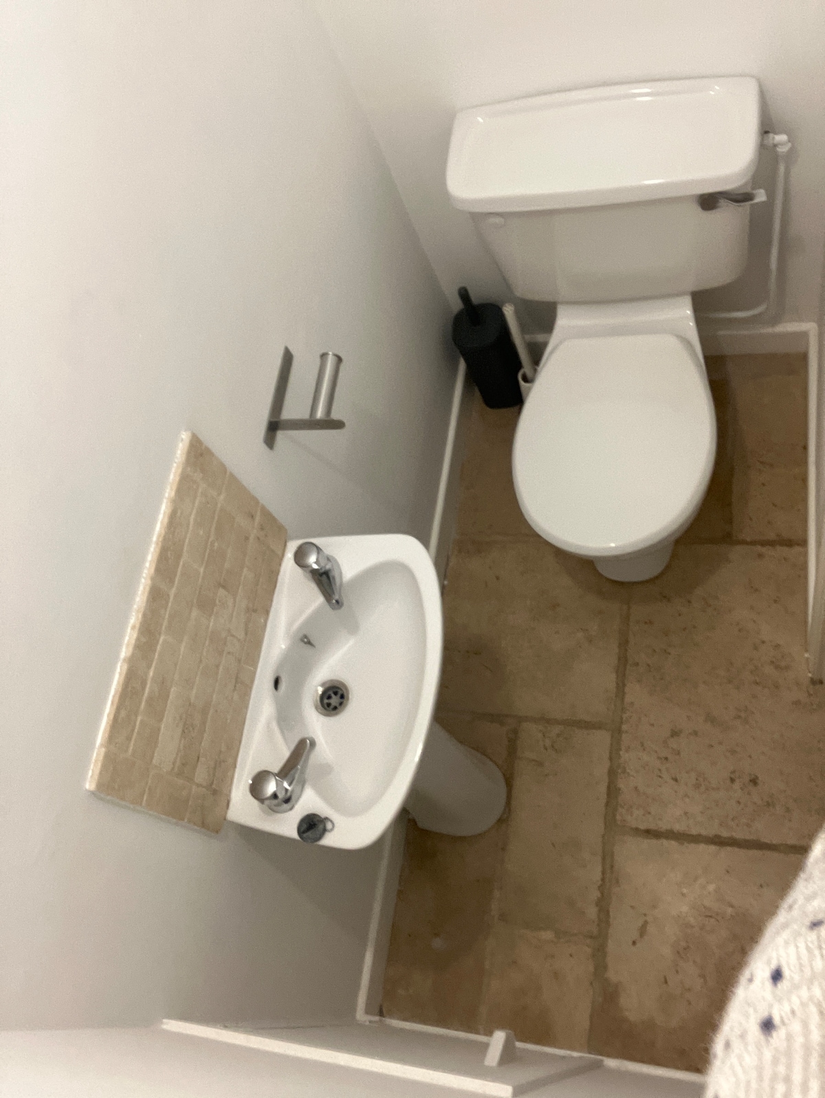 The compact bathroom features a white toilet and a small sink with modern fixtures. The floor is covered in light-colored tiles, providing a clean and minimalist look. A towel bar is mounted on the wall adjacent to the sink.
